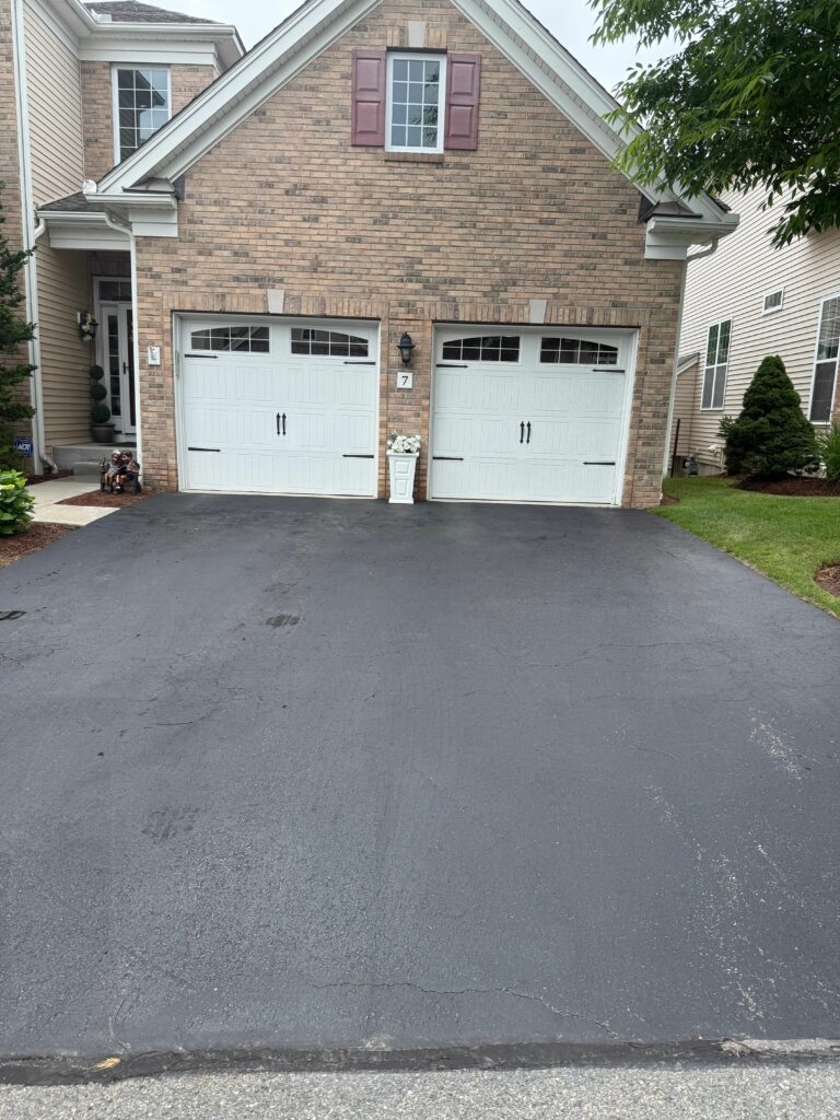 On this Methuen driveway, Eagle Sealcoating chose a premium sealant applied at the correct spread rate, then staked the work off with caution tape so the coating could cure undisturbed and lock out water, UV rays, and winter road salt.